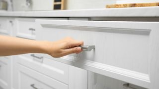 Hand pulling out a white kitchen drawer
