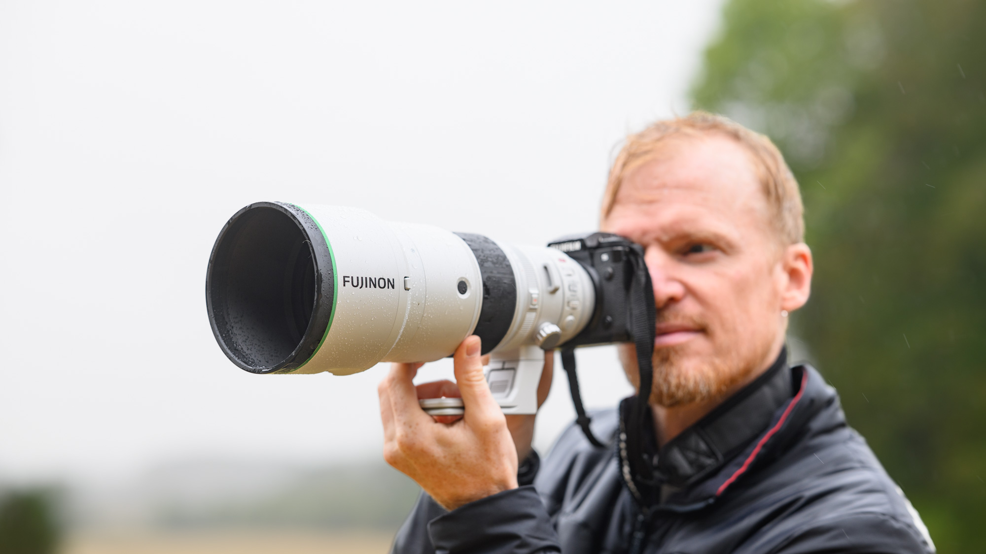 TechRadar Cameras Editor Tim Coleman holding the Fujifilm XF 400mm F4.5 R LM OIS WR telephoto prime lens attached to a Fujifilm X-H2S camera, out in the rain taking pictures