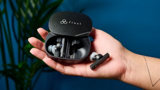 a photograph of black earbuds by final with a long, angular stem and black casing, silicone ear tips, and a black oval case reading 'final' with three decorative hexagons