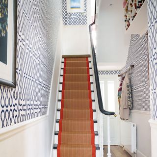 White hallway with geo style bold wallpaper on the walls and a natural flooring stair runner with red edging