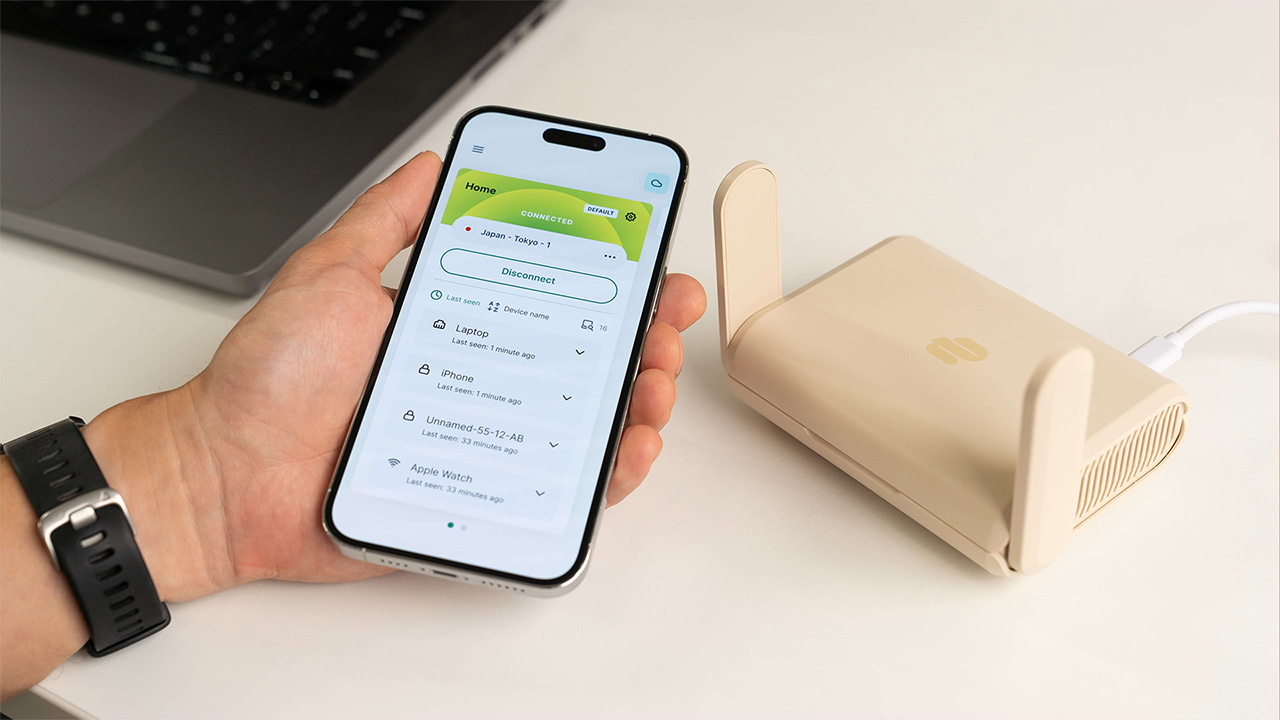 ExpressVPN Aircove Go router on table, with person holding a smartphone next to it. The phone is connected to ExpressVPN