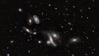 A dark sky speckled with lots of glowing dots. in the foreground, a bunch of hazy blobs of different shapes and sizes.