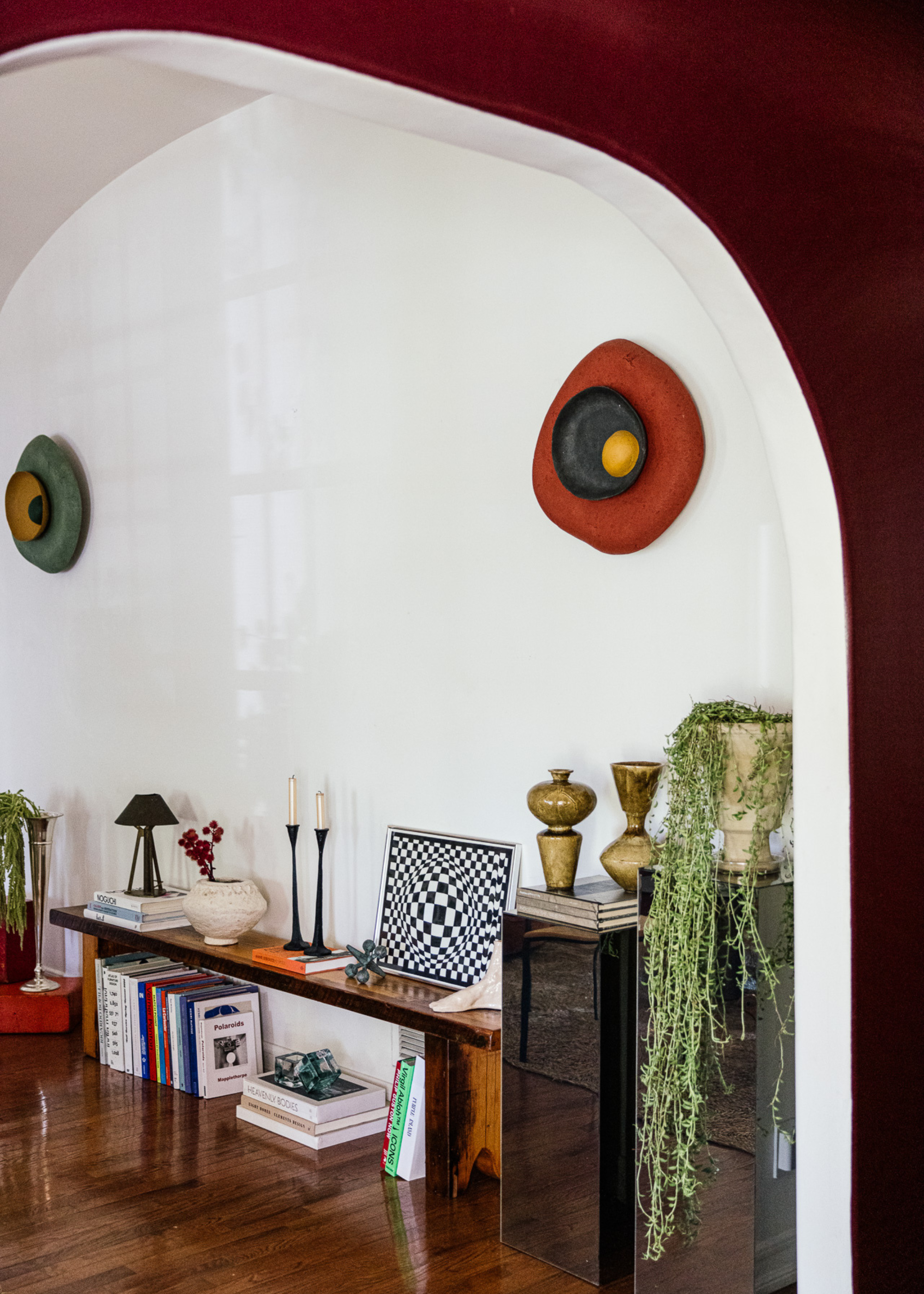 A living room with a low bench with candles, art and ceramics below which lies stacks of books
