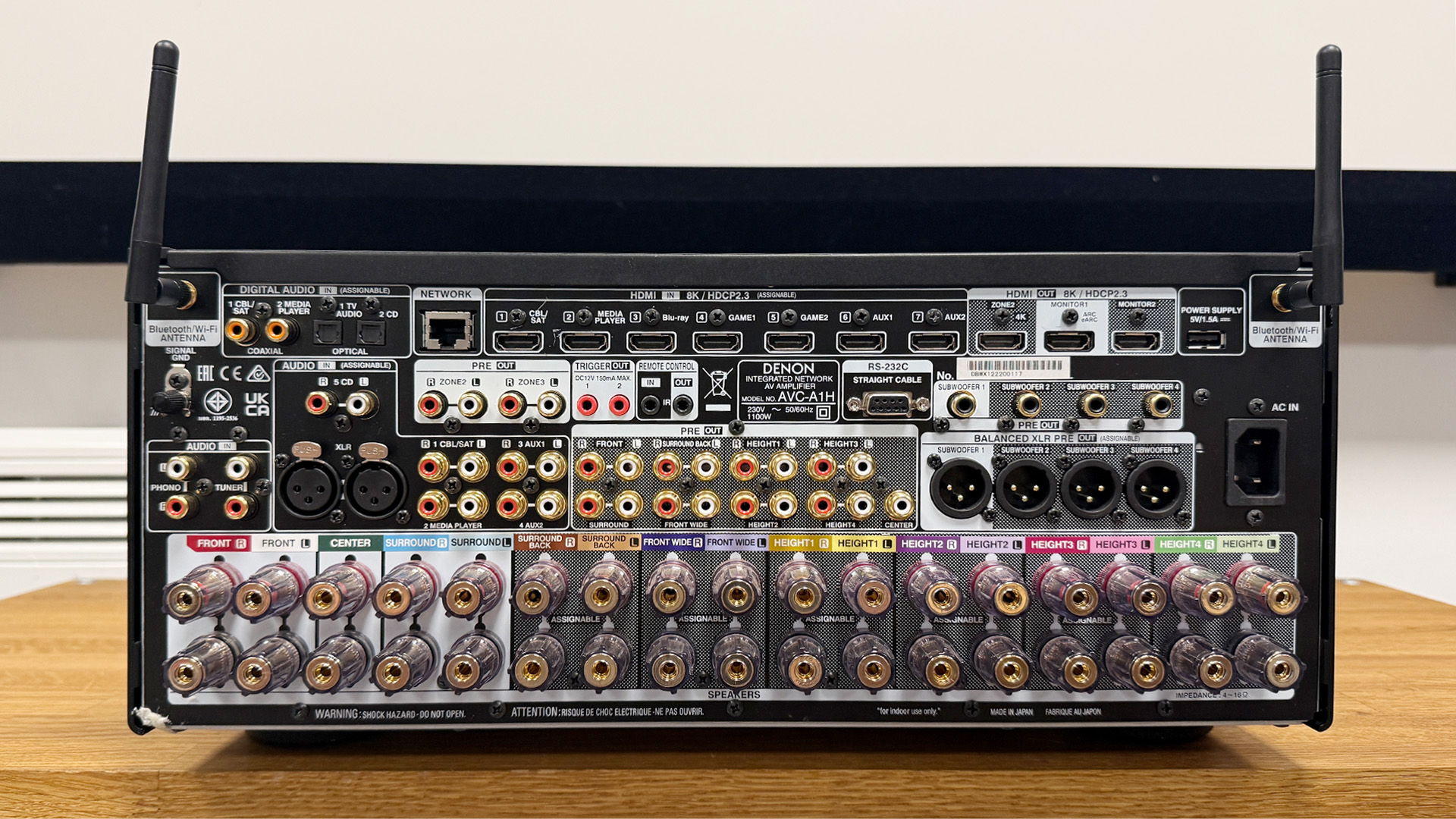Denon AVC-A1H AV amplifier on wooden AV rack showing connections at rear