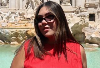 Woman wearing red linen Reformation dress and black sunglasses standing in front of the Trevi Fountain.