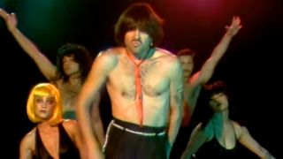 A shirtless man leads a troupe of dancers.