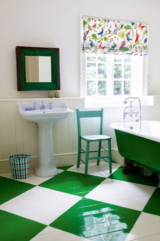 a vintage bathroom with green checkered floor tiles, a small sink and a freestanding green tub