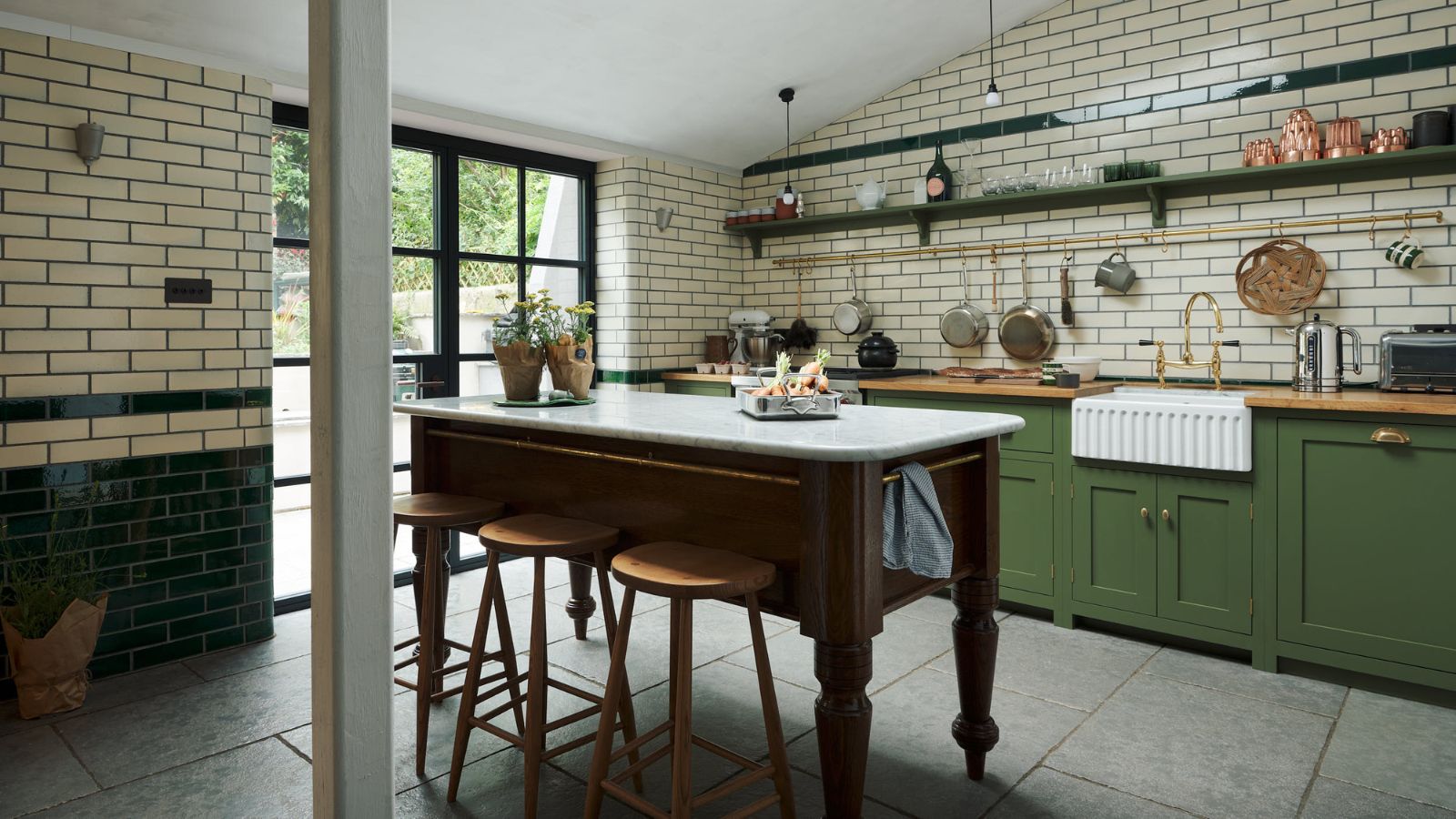 Bright kitchen with cream subway tiles to ceiling, green cabinets and wooden table as island