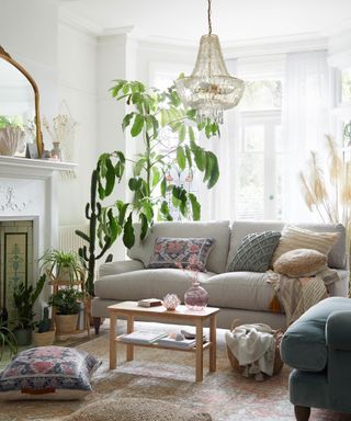 Boho living room with layered textiles, tactile and patterned scatter pillows on neutral comfy sofa, beaded boho ceiling pendant, cacti, and large potted plant.