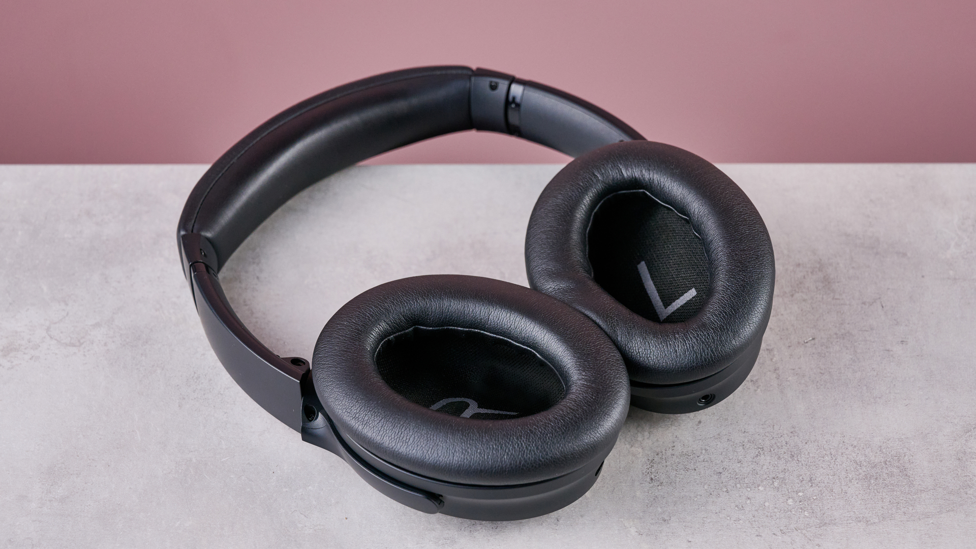 Bose QuietComfort Headphones on a gray surface with a pink background, showing the inside of the earcups