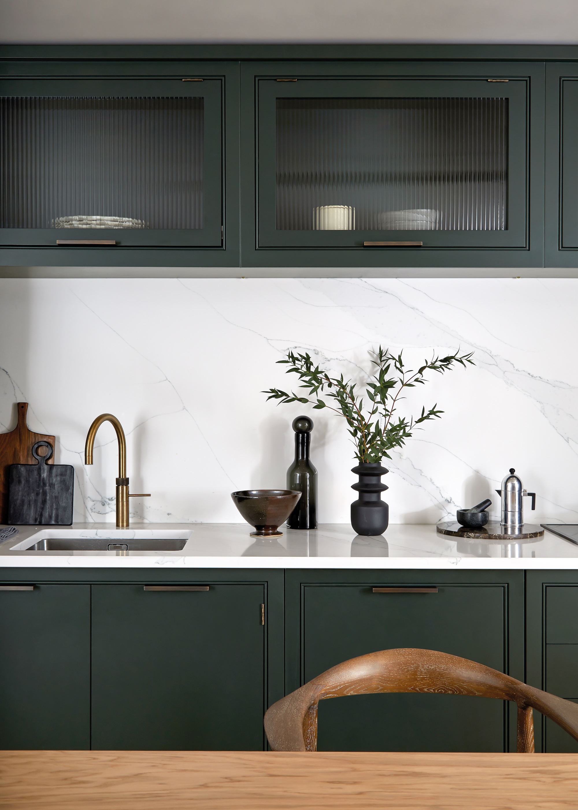 A Quooker tap in brushed bronze shown in a dark green kitchen with white/grey marble worktops and splashback