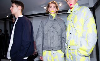 A man standing next to two male mannequins with Chalayan clothing on.