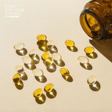 A flat lay of some supplements in a glass jar bottle spilling onto a yellow background