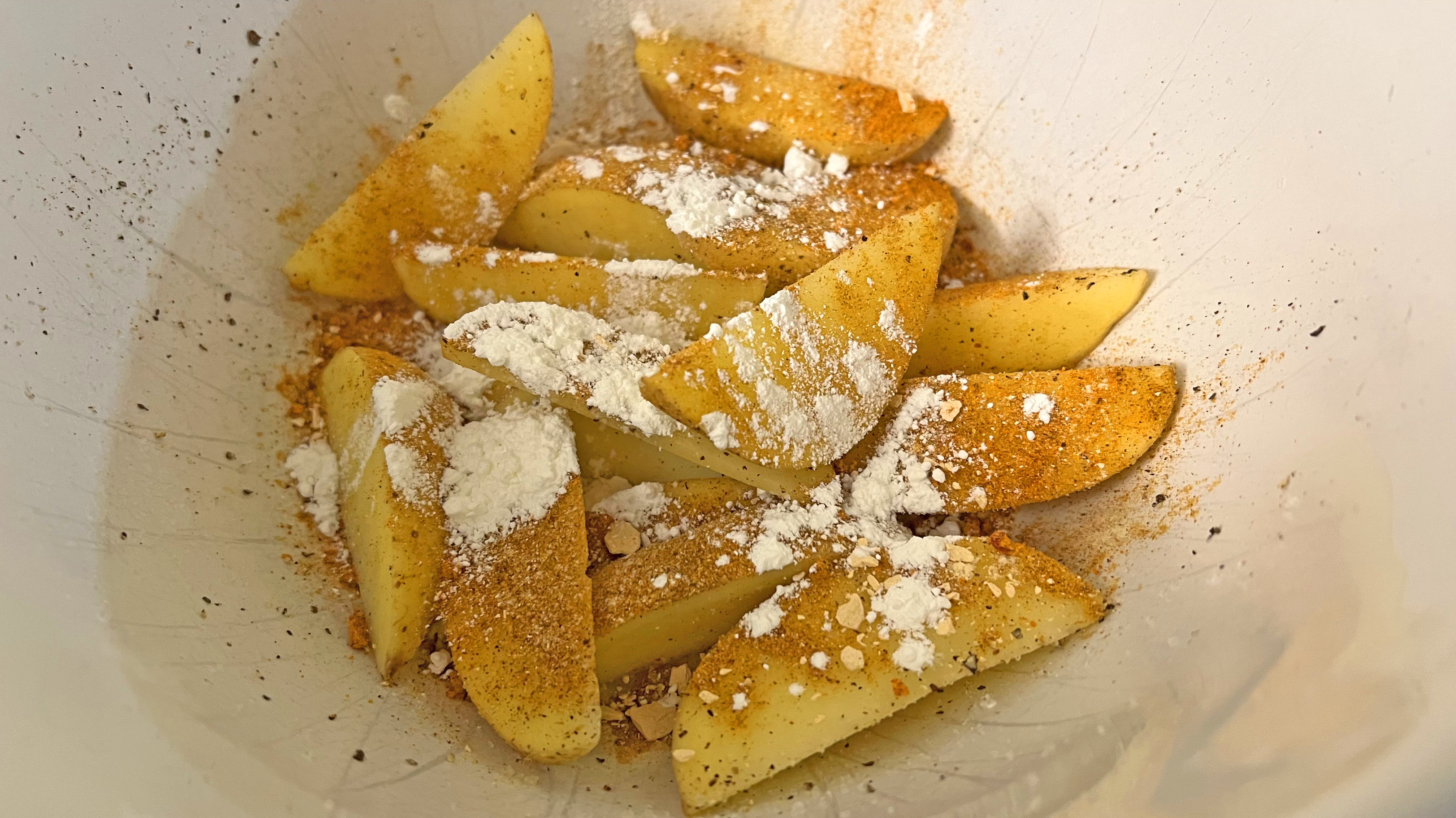 potato wedges in a bowl with cornstarch, pepper salt and paprika seasoning