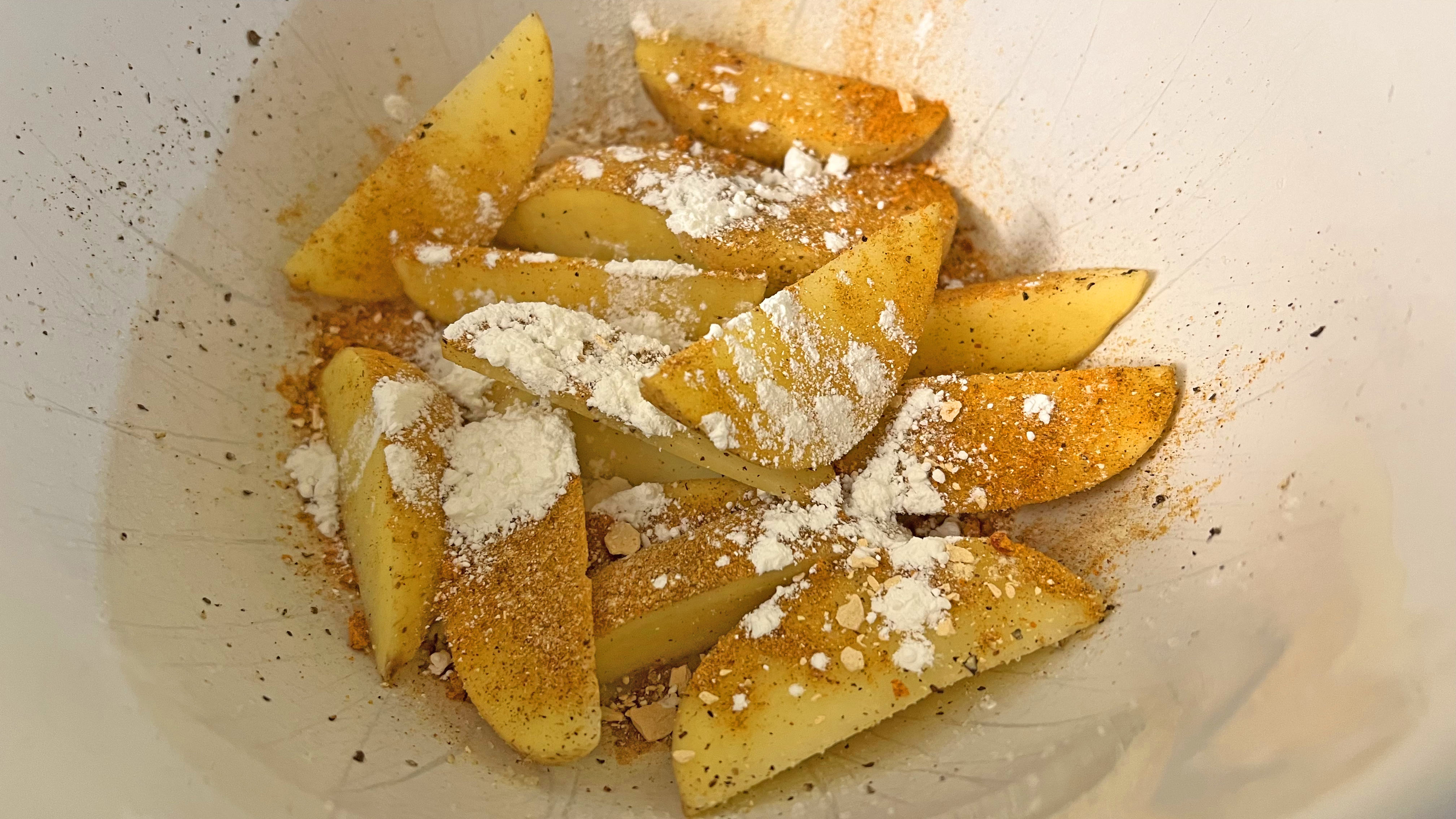 Potato wedges in a bowl with cornstarch, salt, pepper and paprika seasoning