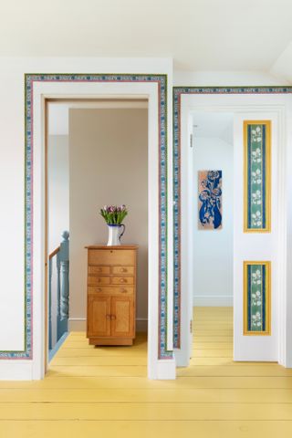 Decorative wallpaper border framing two doorways from a hallway with yellow painted wood floorboards