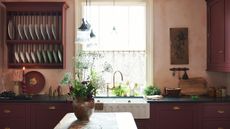 deVOL kitchen in a traditional English style with red cabinetry, pink walls and wood island with vase and flowers 