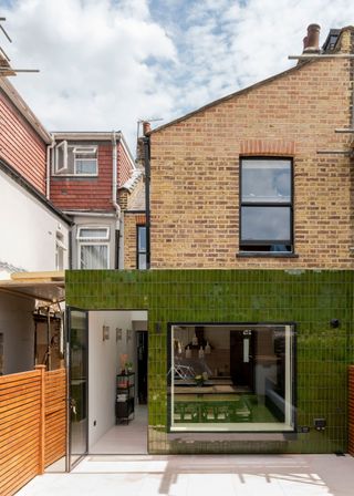 The outside of a home with a kitchen extension. The extension has green tiles outside of it and you can also see into the home.