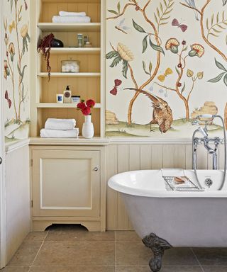 small bathroom with freestanding bath, recessed storage shelves and floral wallpaper
