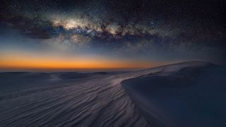 The Milky Way band stretches across the sky above sand dunes. 