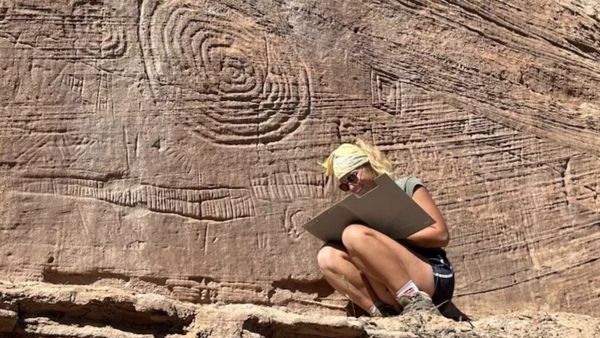 A woman crouches next to petroglyphs. 