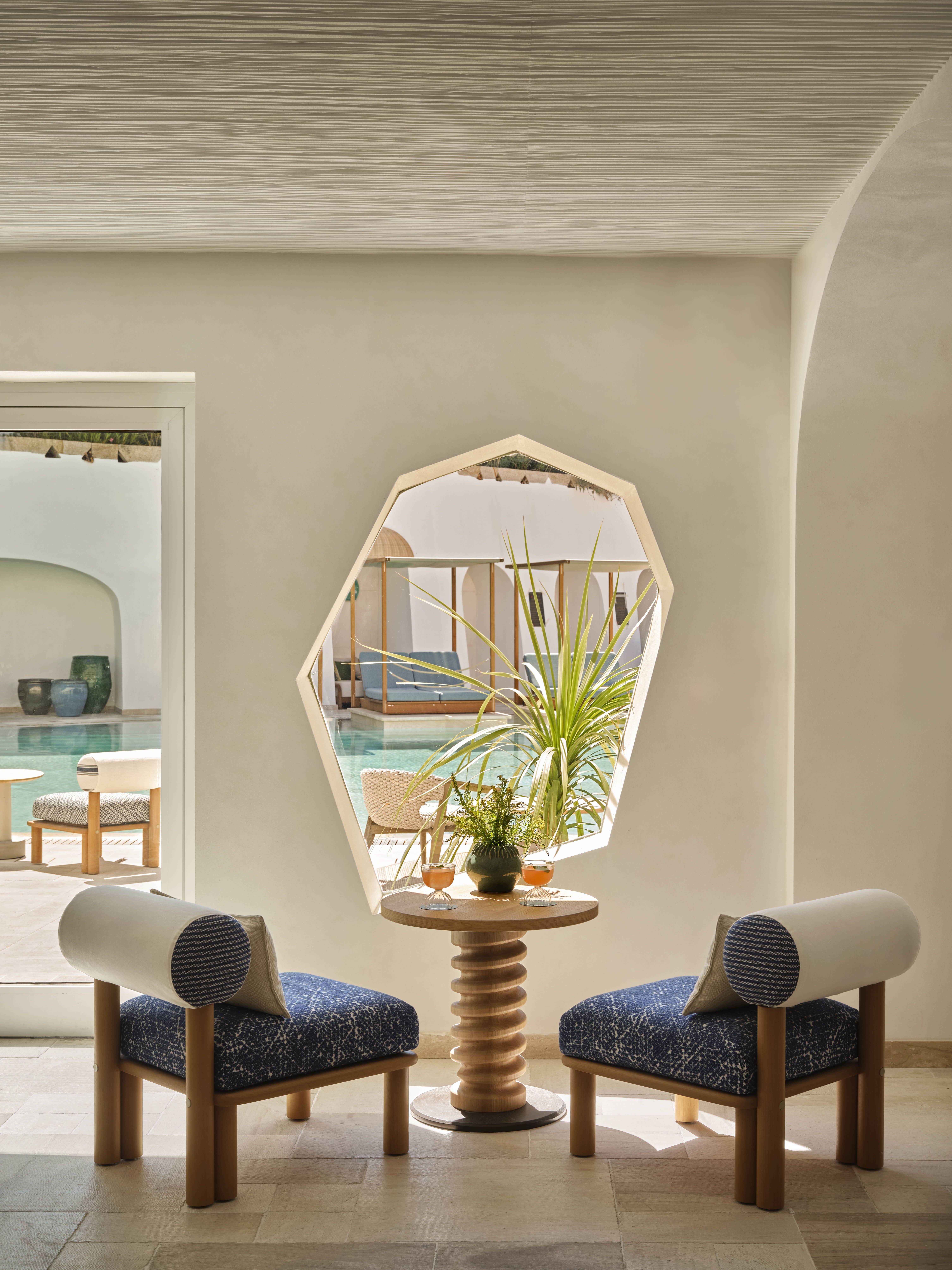 A seaside resort features spectacular, arched ceilings painted in a creamy tone, rattan and wooden furniture in playful silhouettes, turquoise accents, and a panoramic pool.