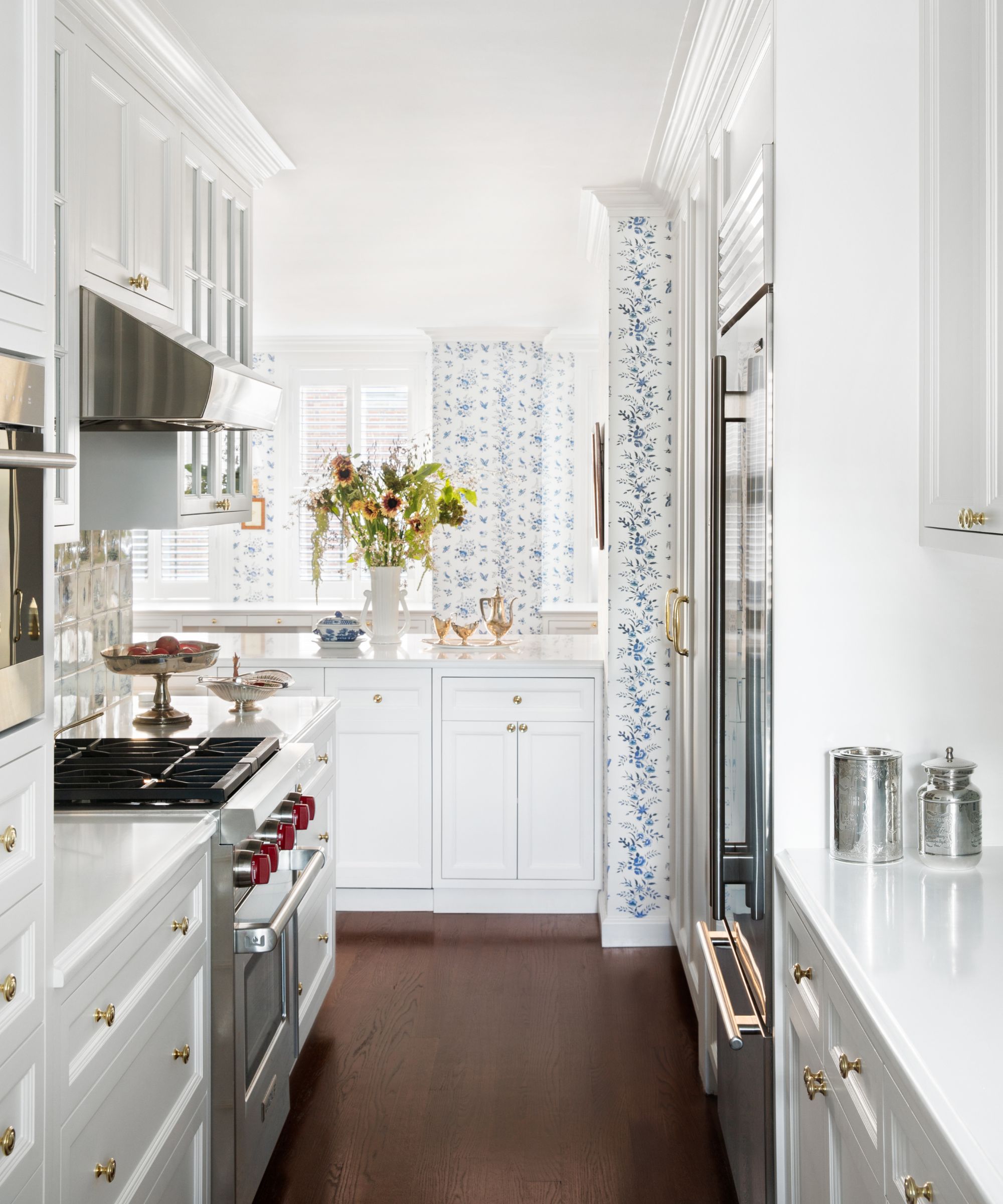 A white L-shaped kitchen with a wood floor and blue and white patterned wallpaper