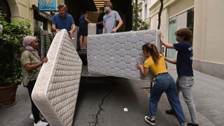 A group of people moving mattresses into a truck parked on the roadside