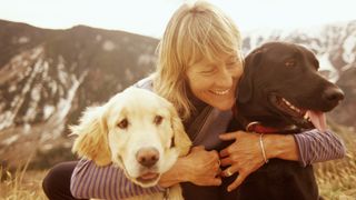 Mature woman hugging her two dogs with mountain in the background
