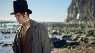 Max Irons in a top hat and coat as Henry Hobday stands by the sea in Miss Austen.