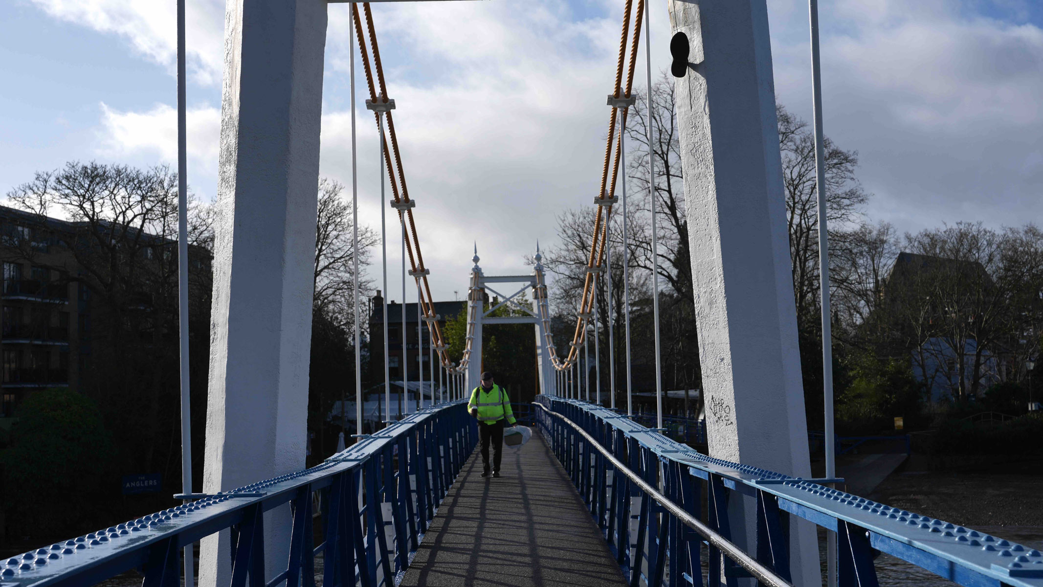 A view across a bridge with a man walking down it wearing a green jacket.