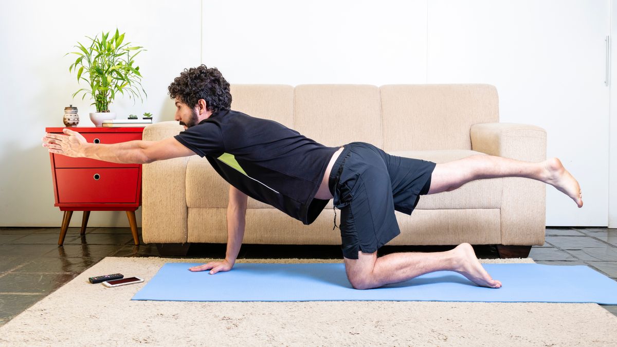 Man performs dead bug exercise on an exercise mat next to a sofa