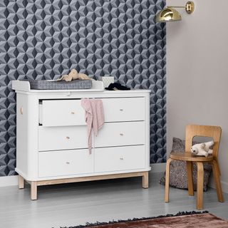 Grey nursery with grey geometric wallpaper and white dresser