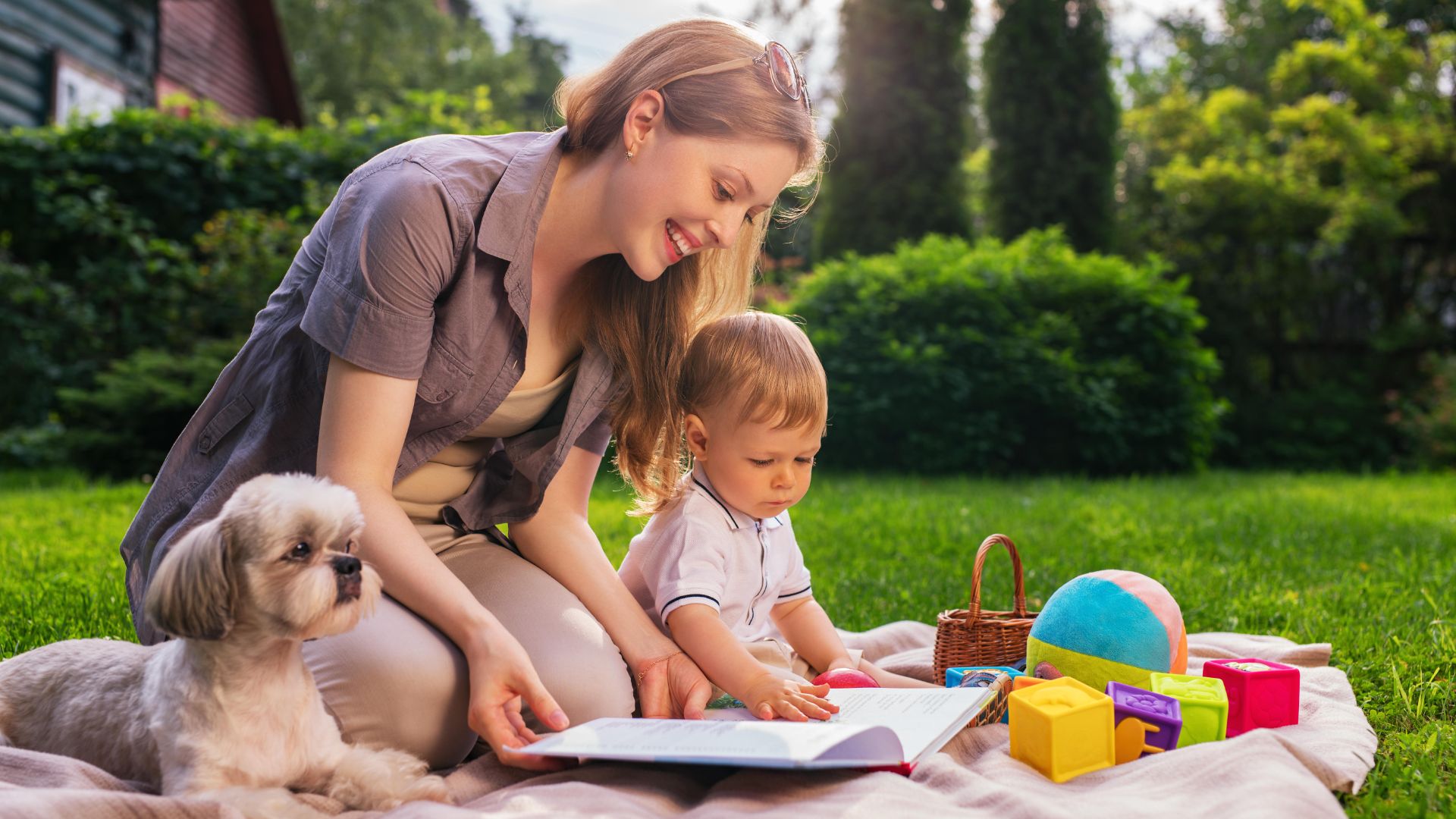 Mother and baby sit reading in the garden with their dog alongside