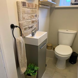 a scandi style cloakroom with grey vinyl flooring, matching vanity sink with a brick splashback, white toilet and pot plant next to the vanity