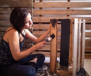 woman with short dark hair painting box made from pallets with black paint