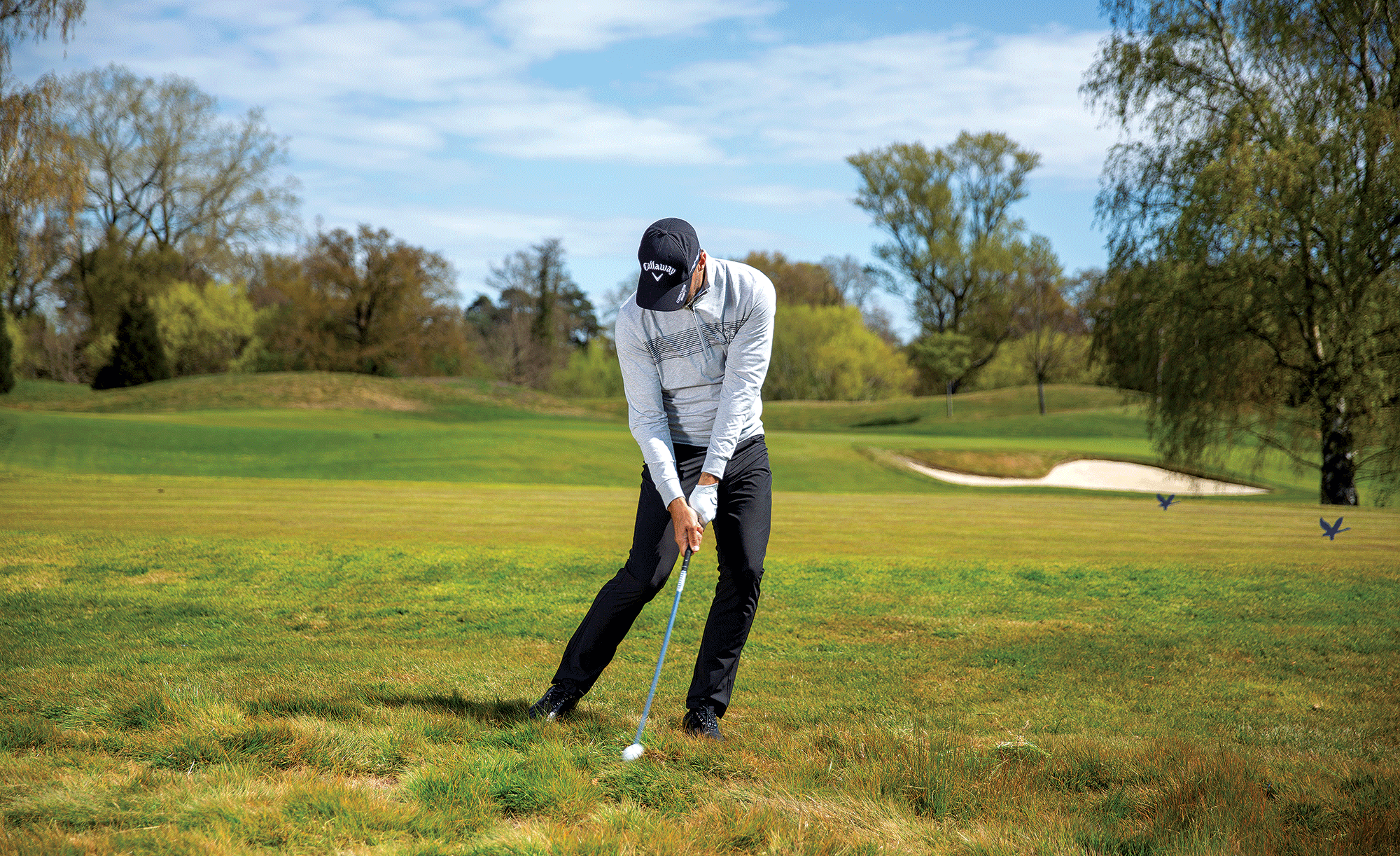 Zane Scotland hitting an iron shot out of the rough, with the ball just popping up at impact with his hands down the grip