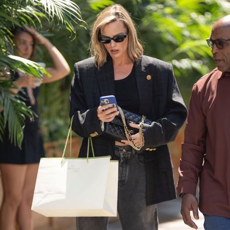 Margot Robbie walks through New York's Chinatown wearing black jeans with two-tone heels and a black oversized blazer.