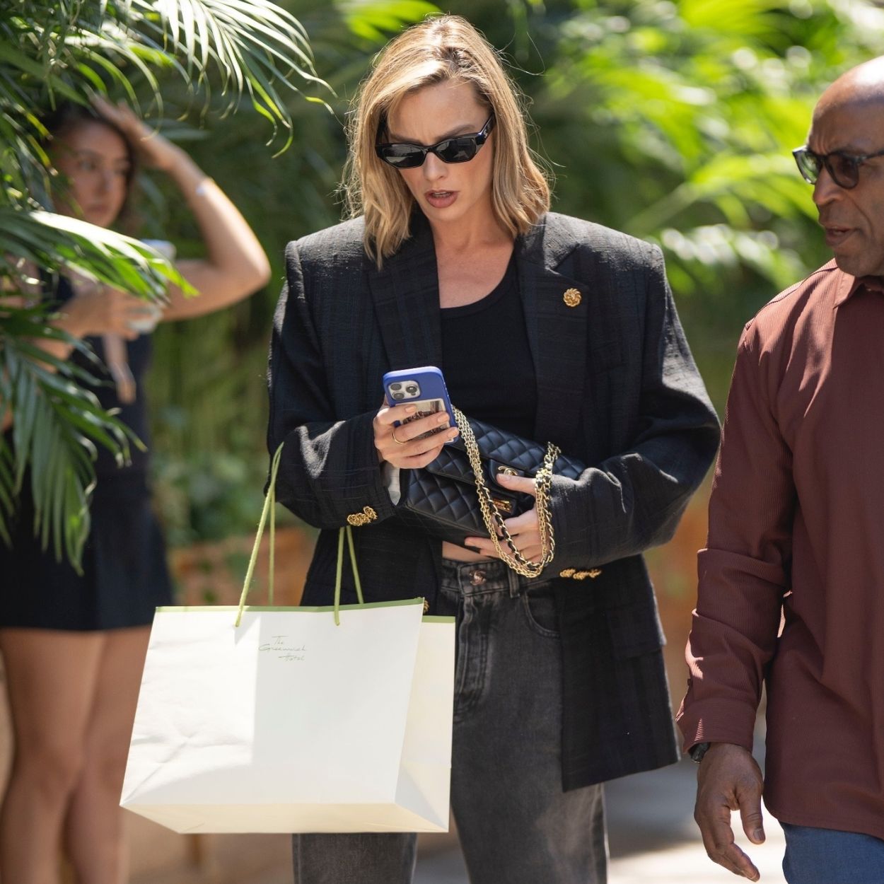 Margot Robbie walks through New York's Chinatown wearing black jeans with two-tone heels and a black oversized blazer.