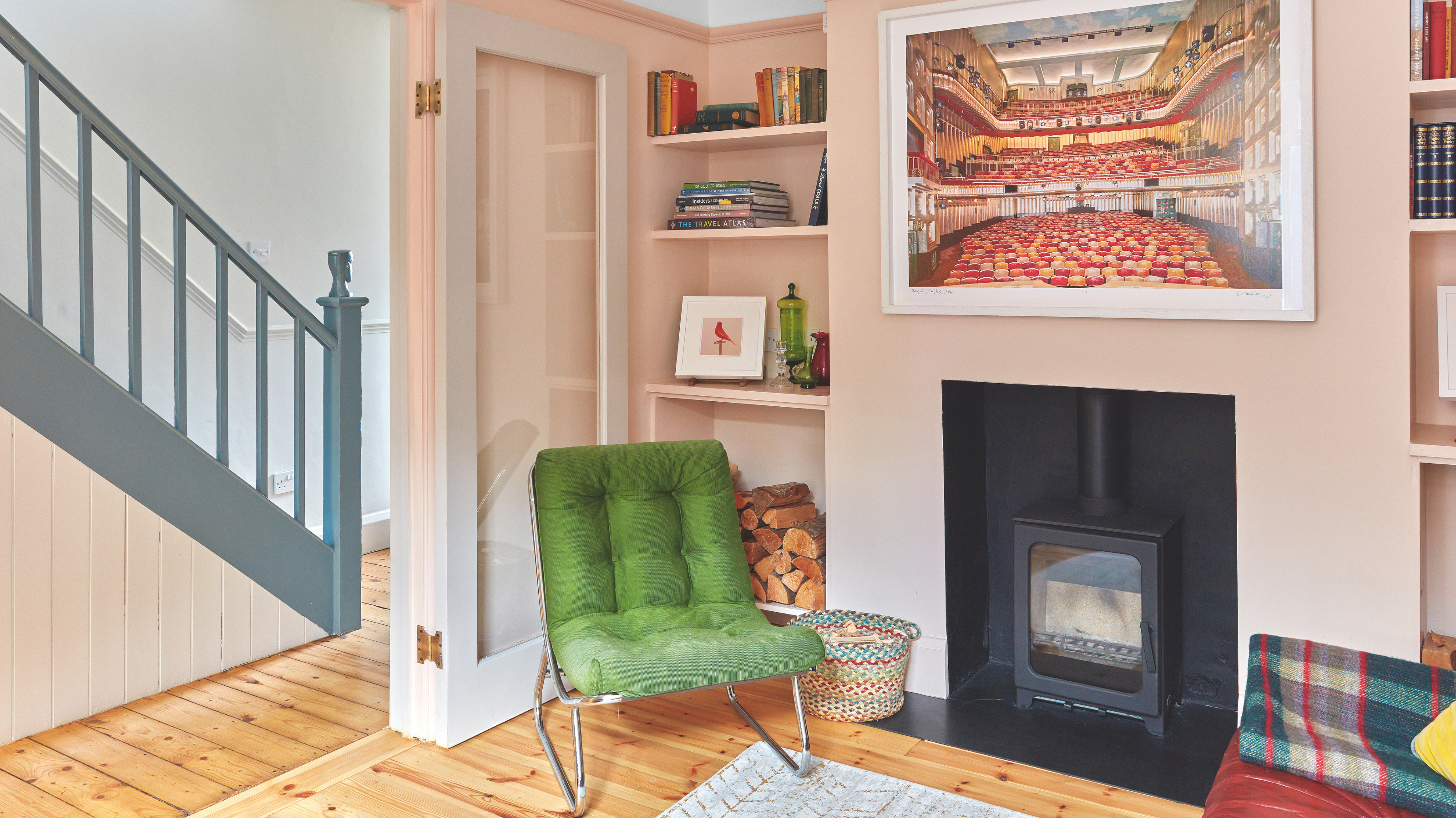 Pale pink living room with log burner and a rich green armchair.
