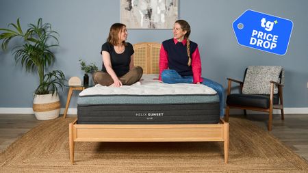Two women sit and chat on the Helix Sunset Luxe mattress. In the top right foreground, there is a Price Drop deals badge to show the mattress is on sale. 