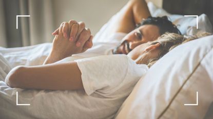 Couple holding hands in bed, wearing white tshirts, representing the snow angel sex position