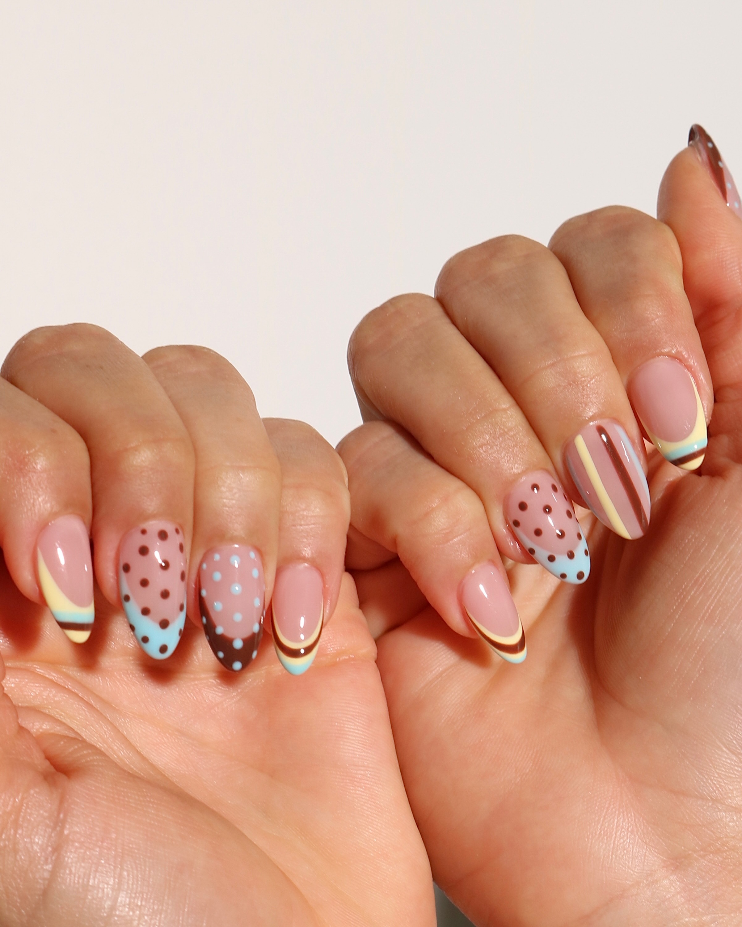 Pink almond nails decorated with baby blue, chocolate brown, and cream stripes, dots, and French tips
