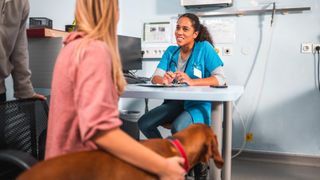 A woman and her dog sit down for a consultation with a veterinarian