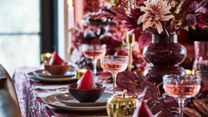 a fall tablescape in shades of red with flowers, coupe glasses, and table settings with pears in bowls