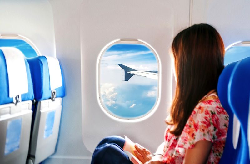 A woman sits in an airplane seat, looking out the window.