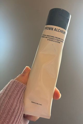 a hand holding grown alchemist cream cleanser tube