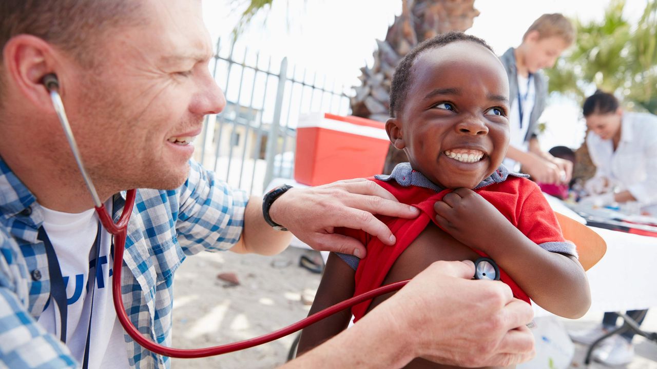 A doctor listens to the heart of a smiling boy.