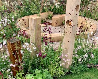 timber posts used as bird feeders and water feature with timber seating behind in 'The Wooden Spoon Garden'