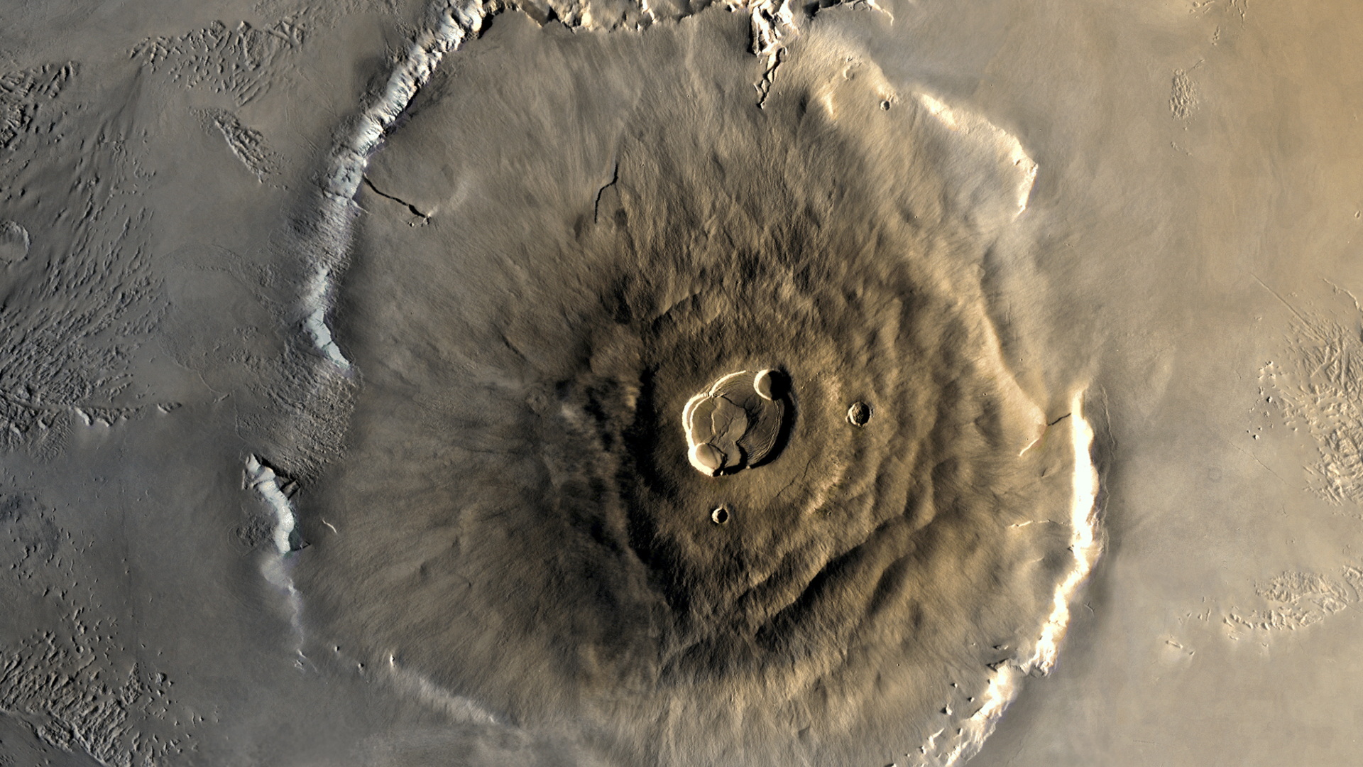 A close up of Olympus Mons on the surface of Mars, its structure a pile of brown lava in a large circular mount on the surface of the planet
